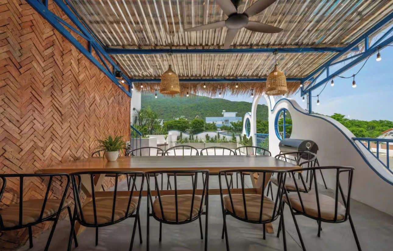 An outdoor dining area with a thatched roof, a long table, and chairs.