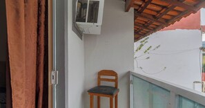 A room with a window, an air conditioning unit, a wooden chair, and a red curtain. - Casa em Angra dos Reis próxima a Praia (Angra dos Reis)