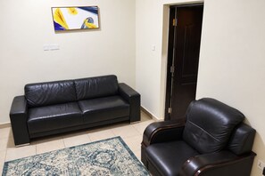 Uma sala de estar com um sofá de couro preto, uma poltrona combinando, um tapete estampado e um quadro na parede.