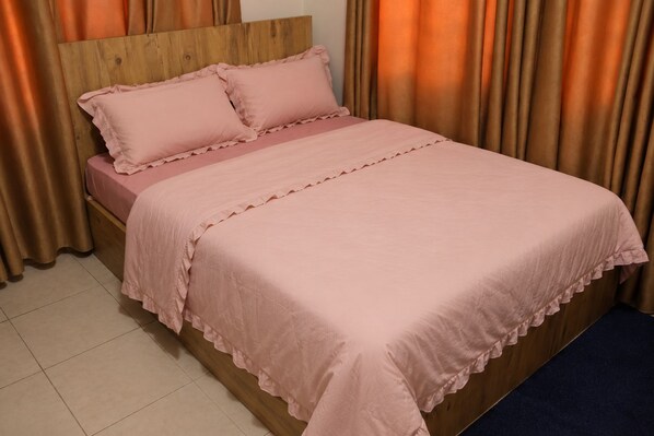 Een bed met een houten hoofdbord, roze beddengoed en gordijnen.