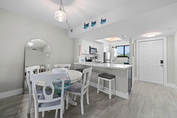 Une cuisine moderne avec des meubles blancs, un îlot central et un coin repas comprenant des chaises blanches et une table ronde.