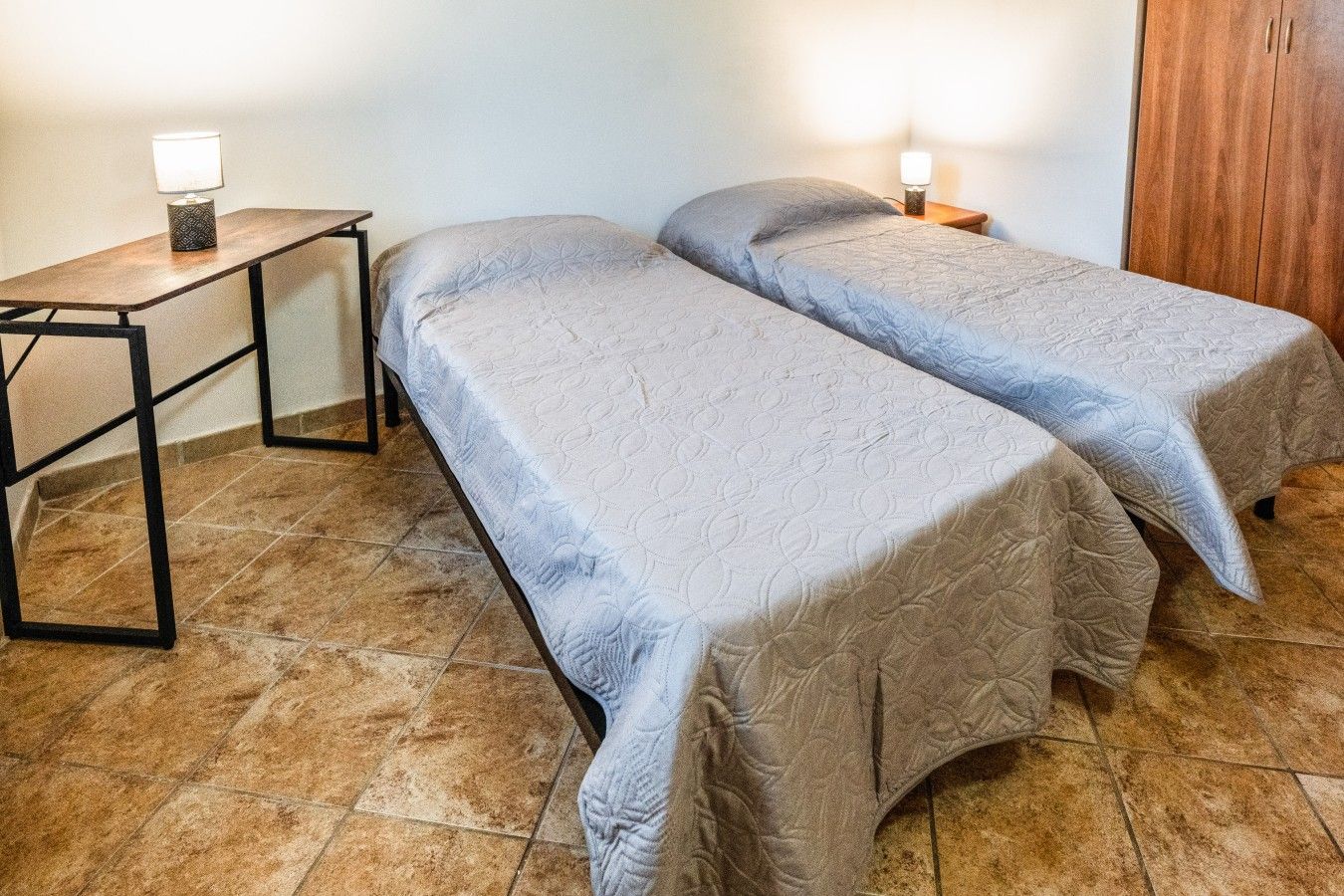 Une chambre avec deux lits, une table de chevet, une lampe et une armoire.