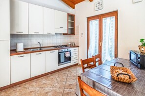Une cuisine avec des meubles blancs, une cuisinière et une table à manger avec des chaises.