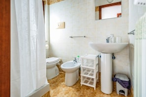Ein Badezimmer mit Toilette, Bidet, Waschbecken und einem Spiegel an der Wand.