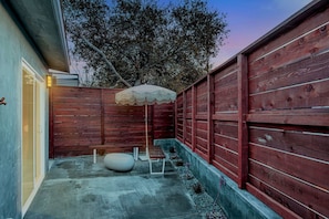 A backyard with a wooden fence, a concrete patio, a white bench, and a white umbrella. - Near Legoland & Beaches | Prime Vista Monthly Stay (Vista)