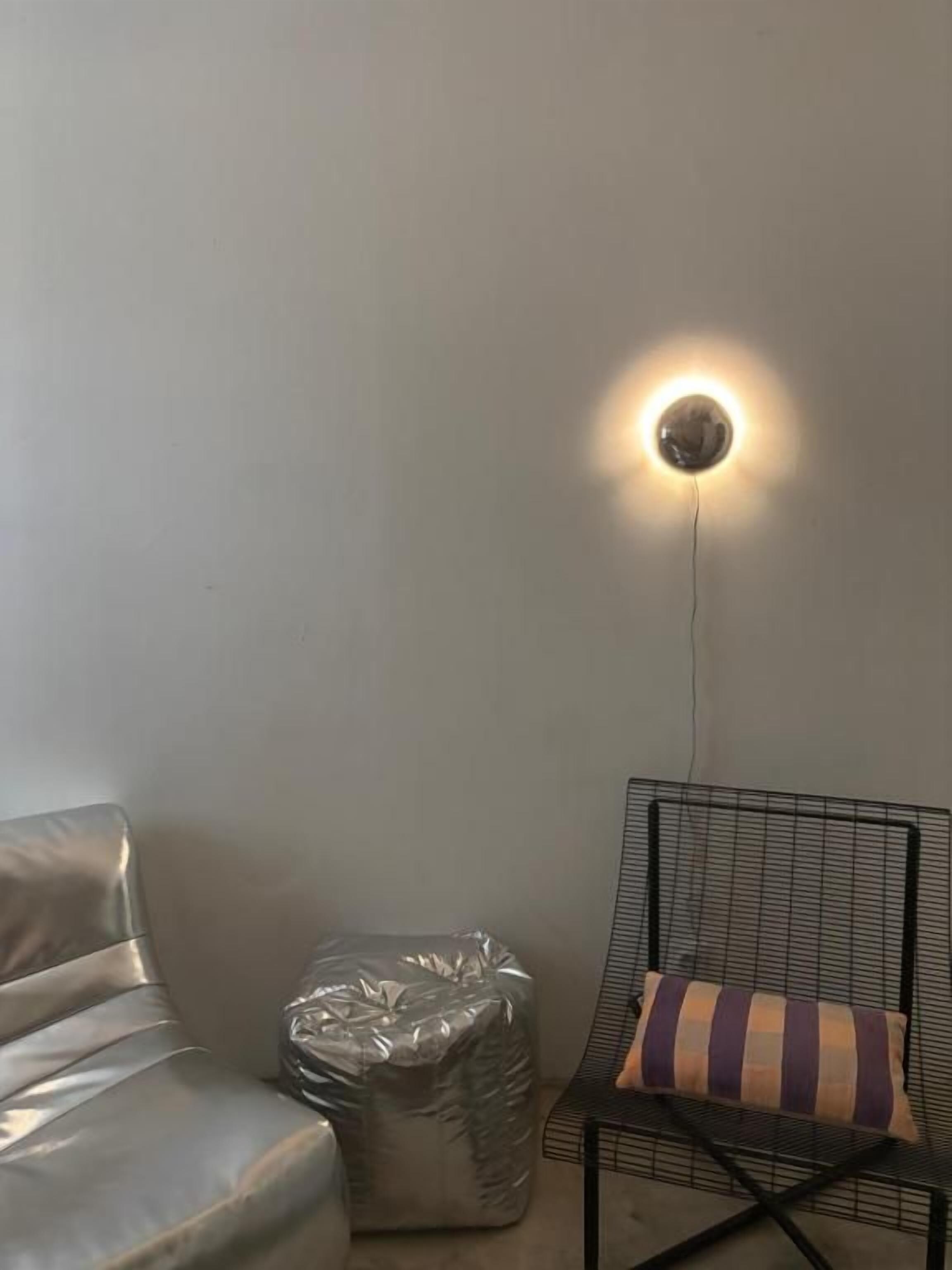 A room with a metal-framed chair, a cushioned ottoman, and a wall-mounted light fixture.