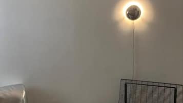A room with a metal-framed chair, a cushioned ottoman, and a wall-mounted light fixture.