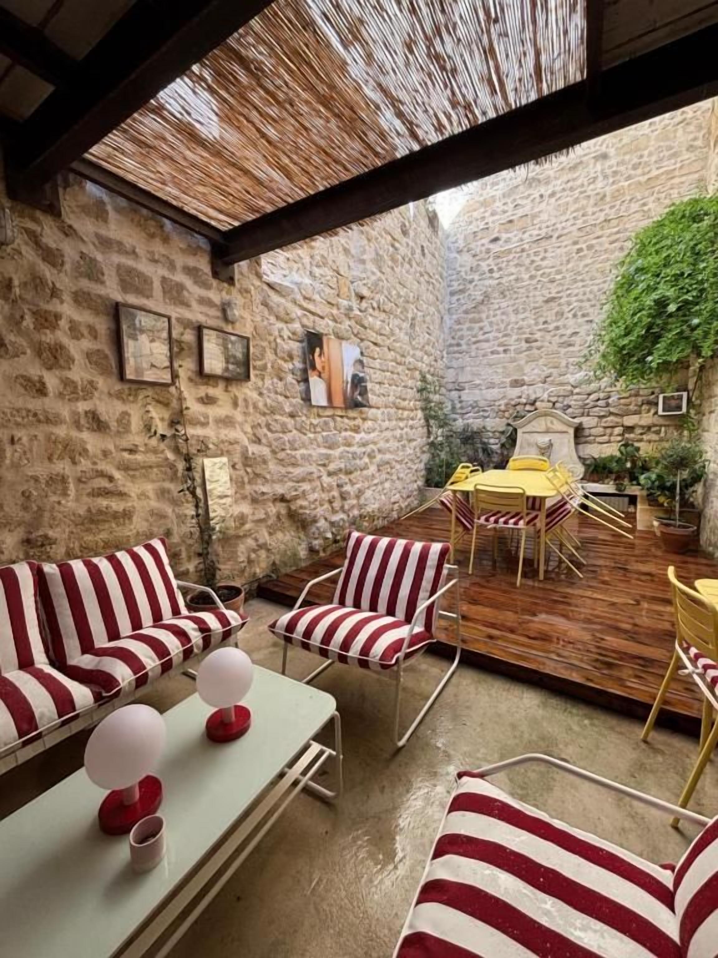 A covered outdoor seating area with striped furniture, a table, and a yellow chair.