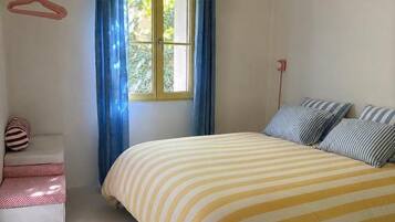 A bedroom with a bed, a window with curtains, a hanging light fixture, and a small bedside table.