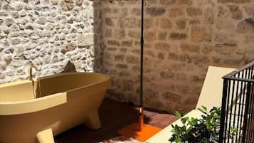 A stone wall, a bathtub, a checkered floor, a straw umbrella, and potted plants.