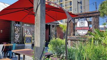 An outdoor seating area with red umbrellas, a wooden post, and a sign for 'PIZZAHYENA' with a logo.