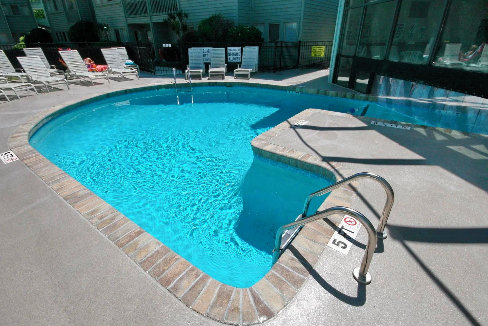 Une piscine équipée d’un escalier en métal, de chaises longues et d’un panneau indiquant qu’il est interdit de plonger.