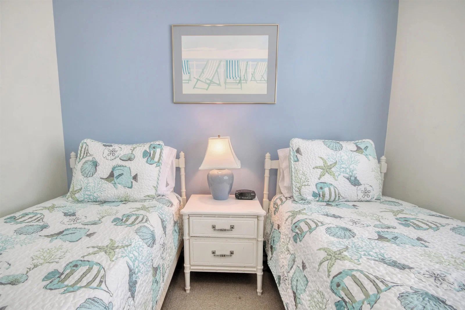 A bedroom with two beds, each with a matching headboard and footboard, a bedside table with a lamp, and a framed picture on the wall.