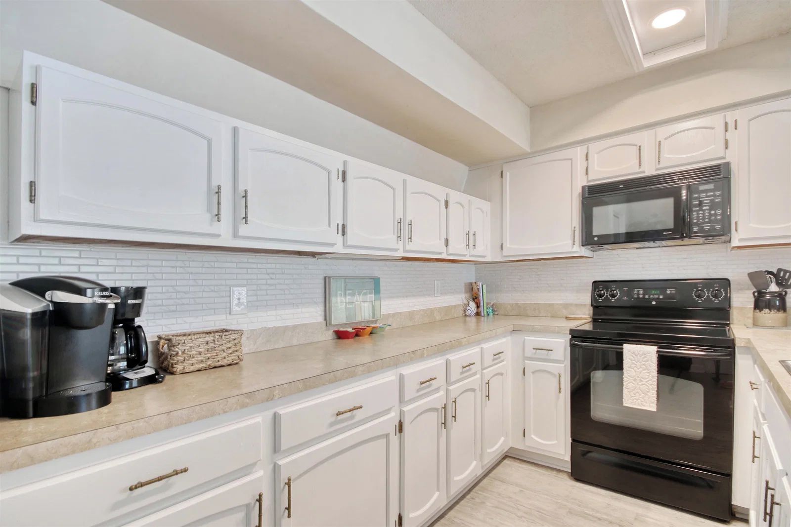 A kitchen with white cabinets, a black microwave, a coffee maker, and a tiled backsplash.