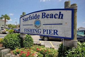 A sign for Surfside Beach Fishing Pier with a clear view of the surrounding parking area and greenery. - Cape Coddages 205 · Oceanfront 2BR Surfside Beach (Surfside Beach)