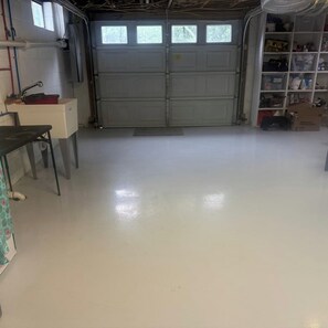Eine Garage mit weißer Tür, einer Werkbank und Regalen mit verschiedenen Gegenständen.