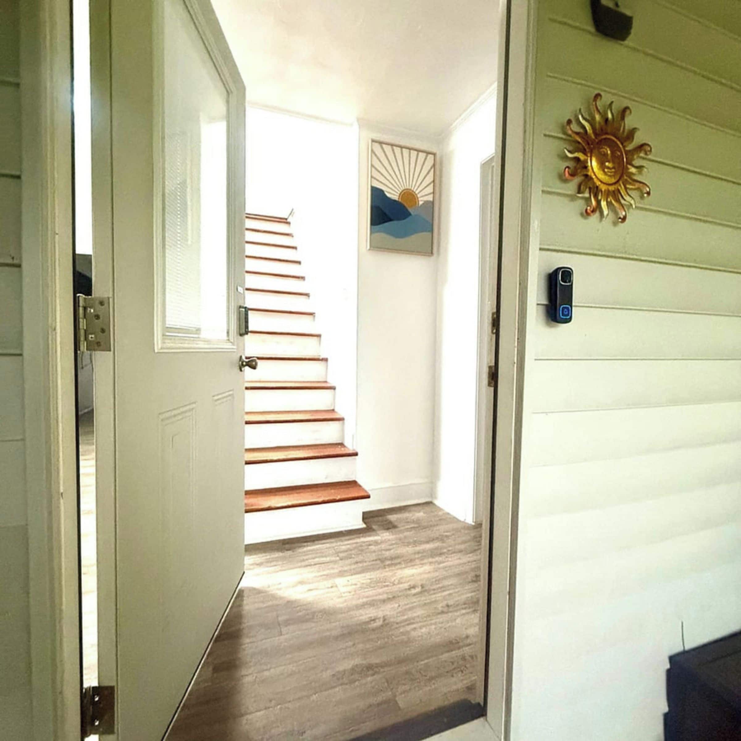 A hallway with a wooden staircase leading to a room, a door with a handle, and a wall-mounted light switch.