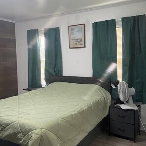 A bedroom with a bed, a bedside table, a fan, and a window with curtains. - Welcoming 7-bedroom house with AC in charming Salisbury (Salisbury)