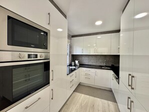 A modern kitchen with white cabinetry, stainless steel appliances, and a black countertop. - Vilamoura Marina Beach 2 by Homing (Loulé)