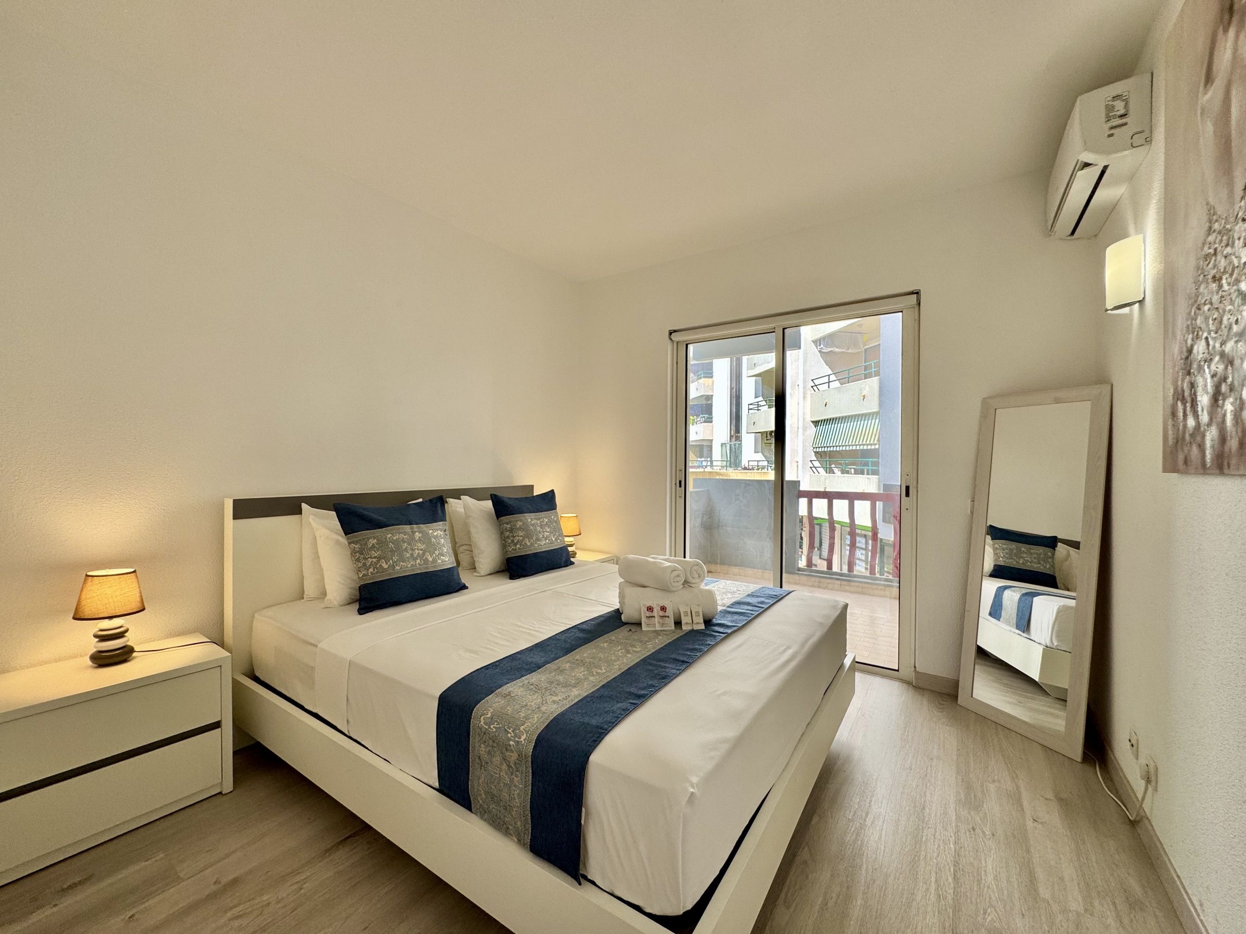 Habitación de hotel con cama, mesita de noche, lámpara y vistas al exterior.
