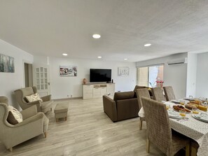 A modern living room with a flat-screen TV, sofas, a dining table set for breakfast, and artwork on the walls. - Vilamoura Marina Beach 2 by Homing (Loulé)