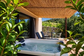 Ein Whirlpool mit Liegestühlen und einem Tisch, umgeben von Grünpflanzen und einer Steinmauer.