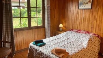 A room with wooden paneling, a bed with a patterned quilt, a bedside lamp, and a window with curtains.