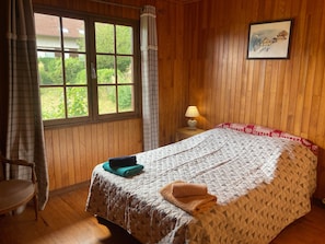 Ein Zimmer mit Holzvertäfelung, einem Bett mit gesteppter Decke, einer Nachttischlampe und einem Fenster mit Vorhängen.