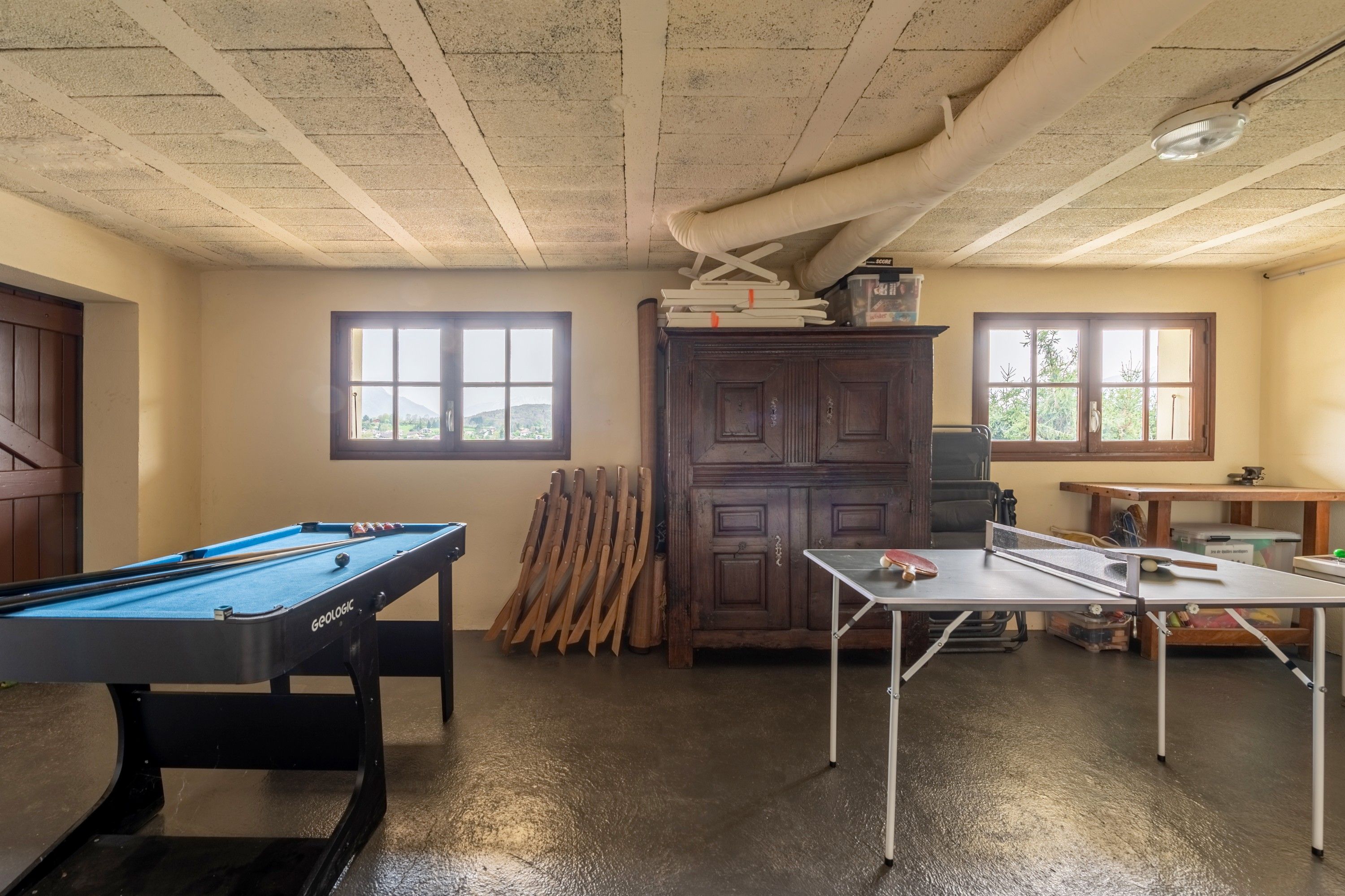 Een kamer met een pooltafel, een tafeltennistafel en een kast met gereedschap.
