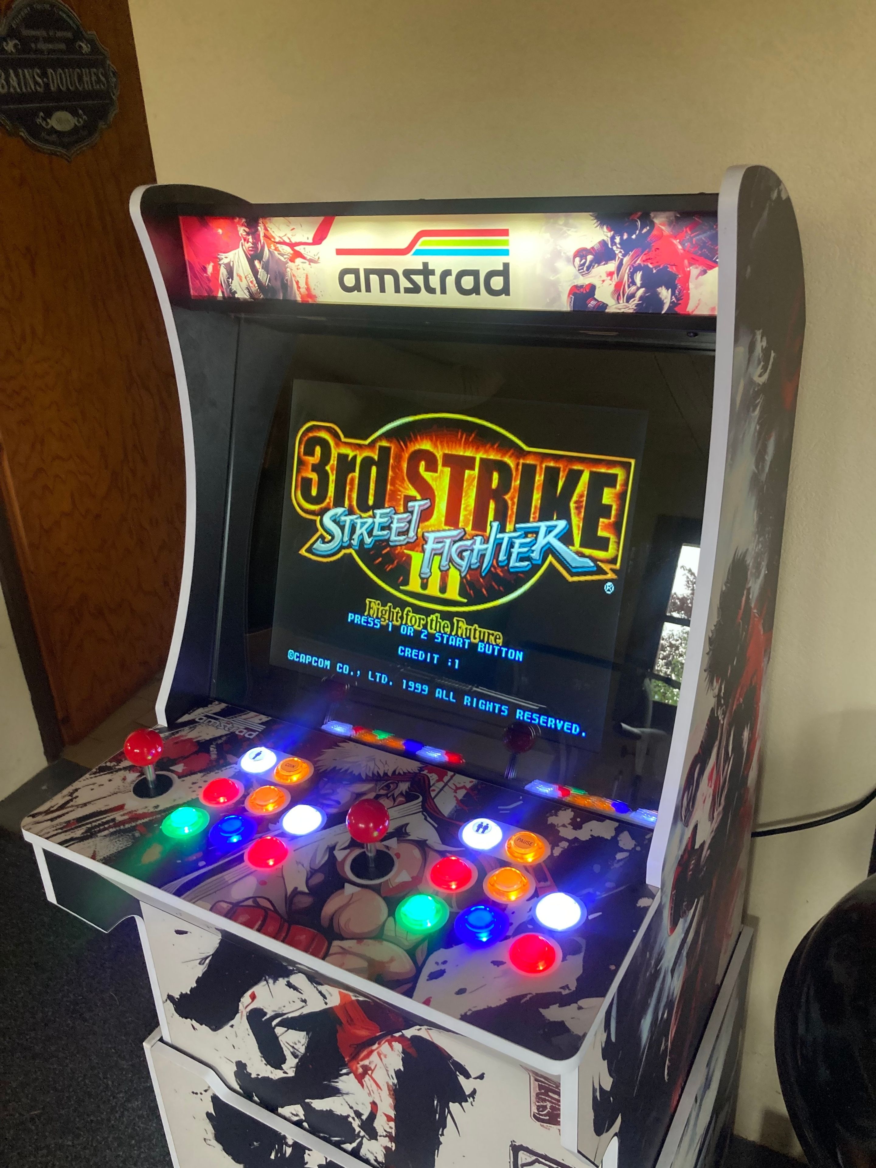 Een spelautomaat met een kleurrijke joystick en een scherm waarop het spel '3rd Strike Street Fighter' wordt getoond.
