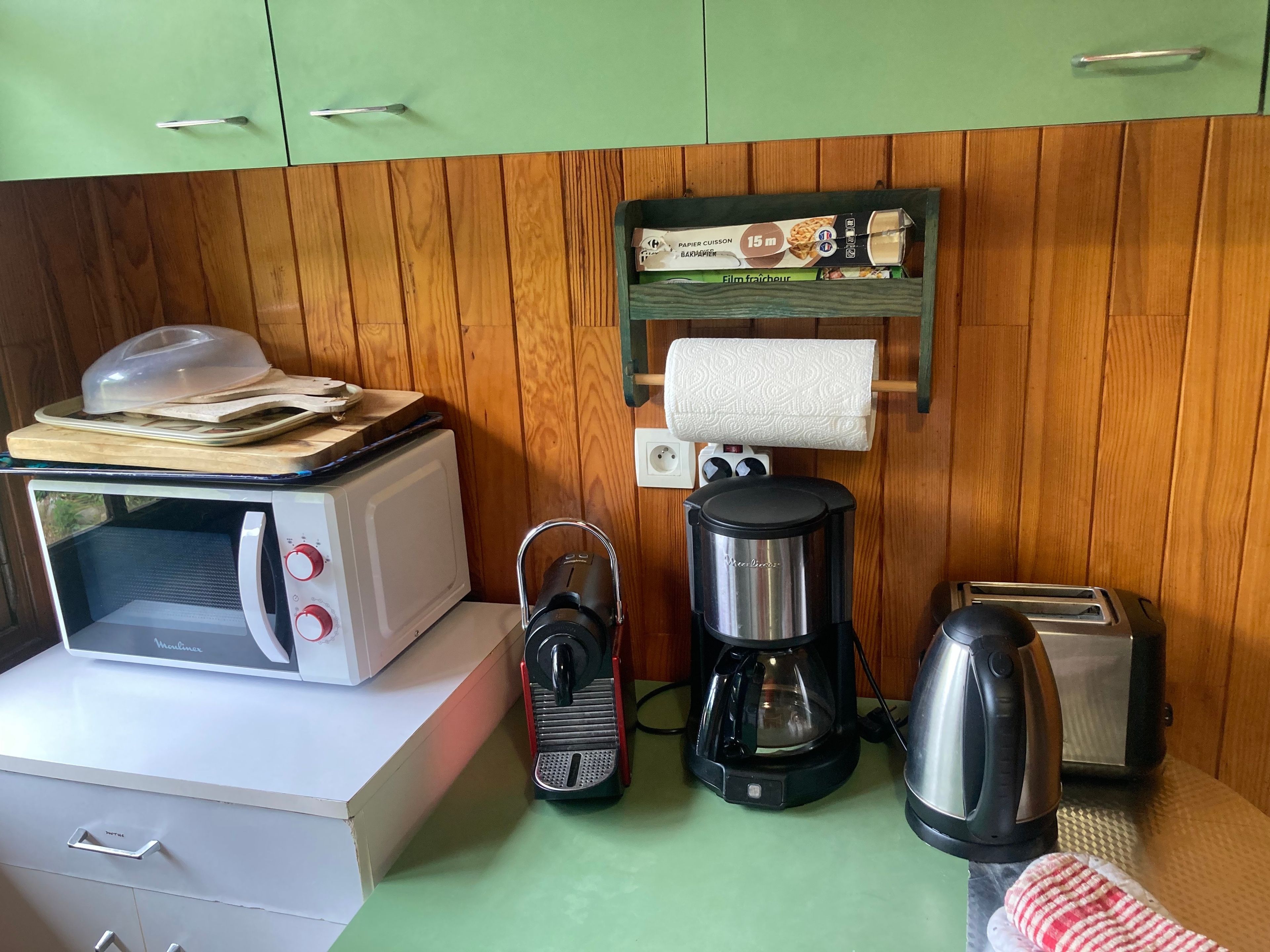 A compact kitchenette with a microwave, toaster, coffee maker, and a small shelf with a box.