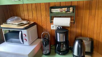 A compact kitchenette with a microwave, toaster, coffee maker, and a small shelf with a box.