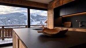 A modern kitchen with a large window overlooking a snowy mountain landscape. - NEW! Chalet Eagle - LES GETS: ski-in/ski-out, fireplace, superb view (Les Gets)