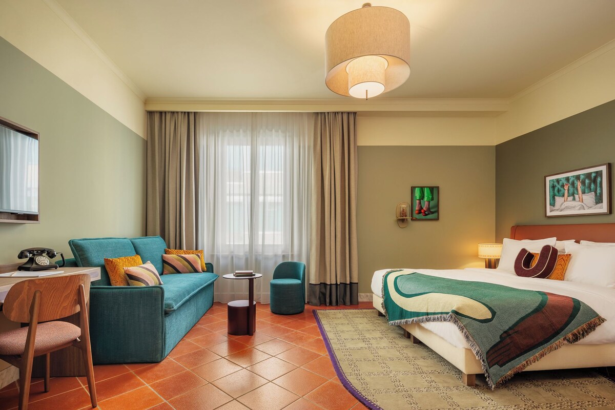 Een hotelkamer met een bed, een slaapbank, een stoel, een klein tafeltje en een lamp.
