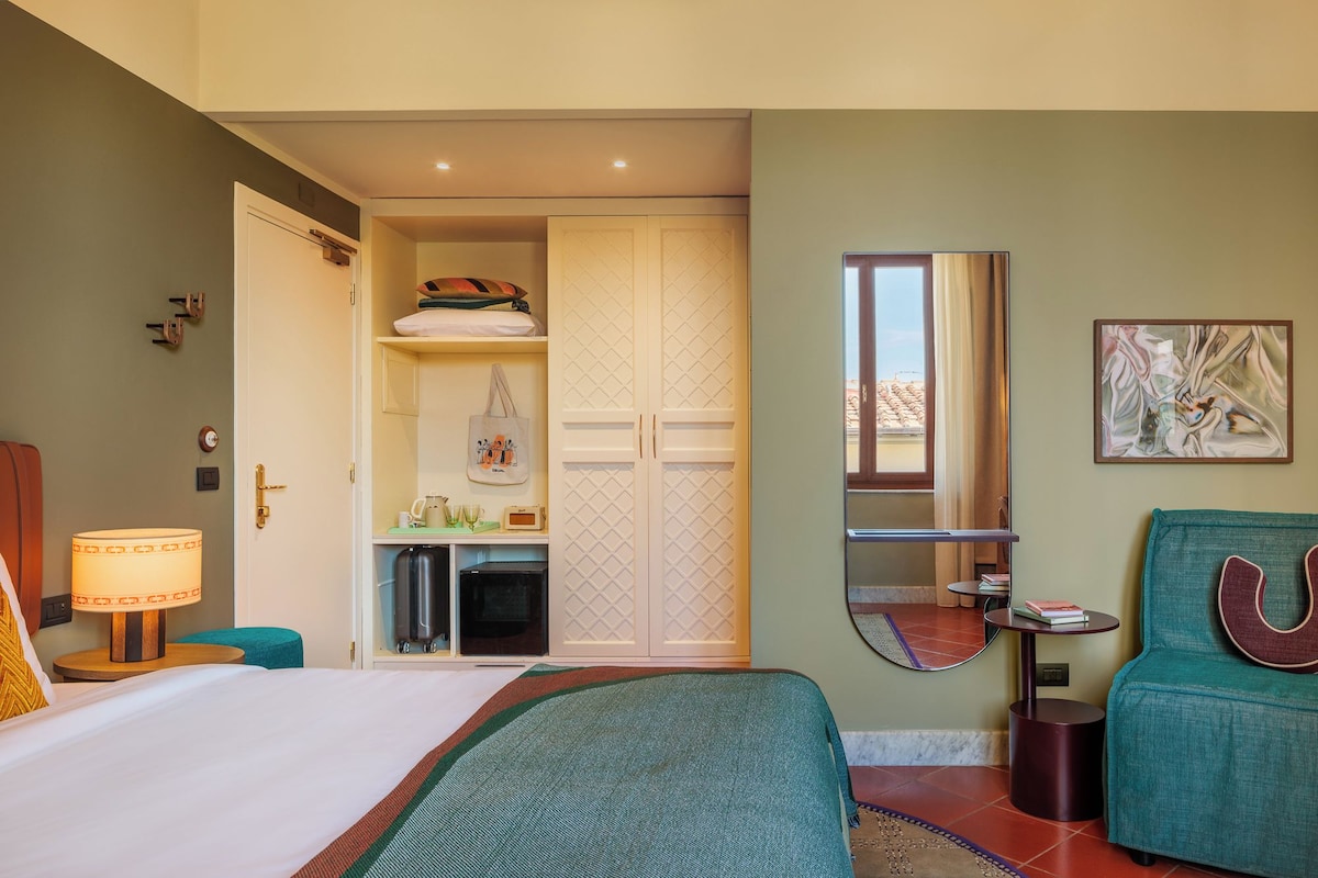 Een hotelkamer met een bed, een bureau, een stoel, een kledingkast, een spiegel en een schilderij.