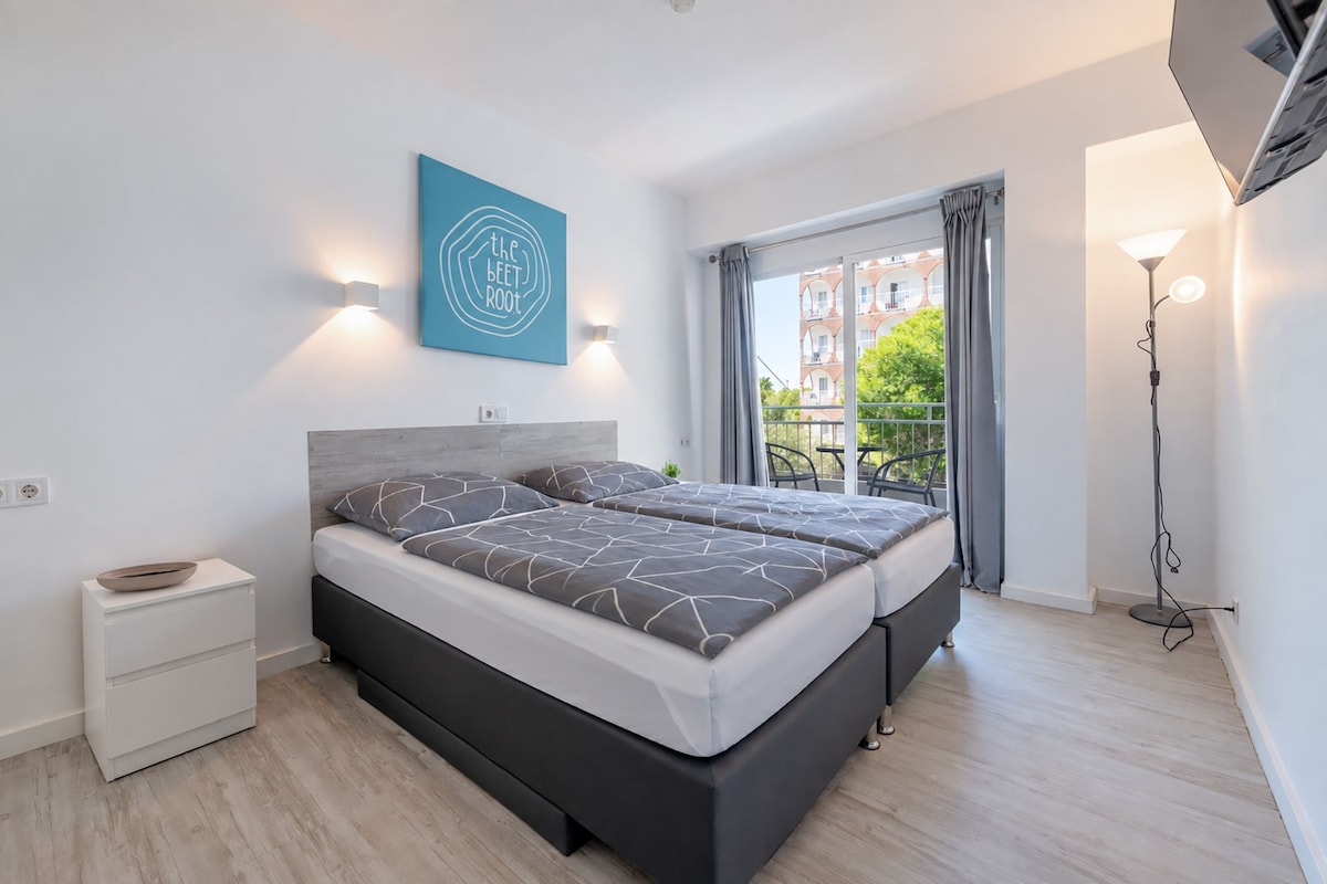 Quarto moderno com cama, mesas de cabeceira, uma obra de arte na parede e vista para o exterior.