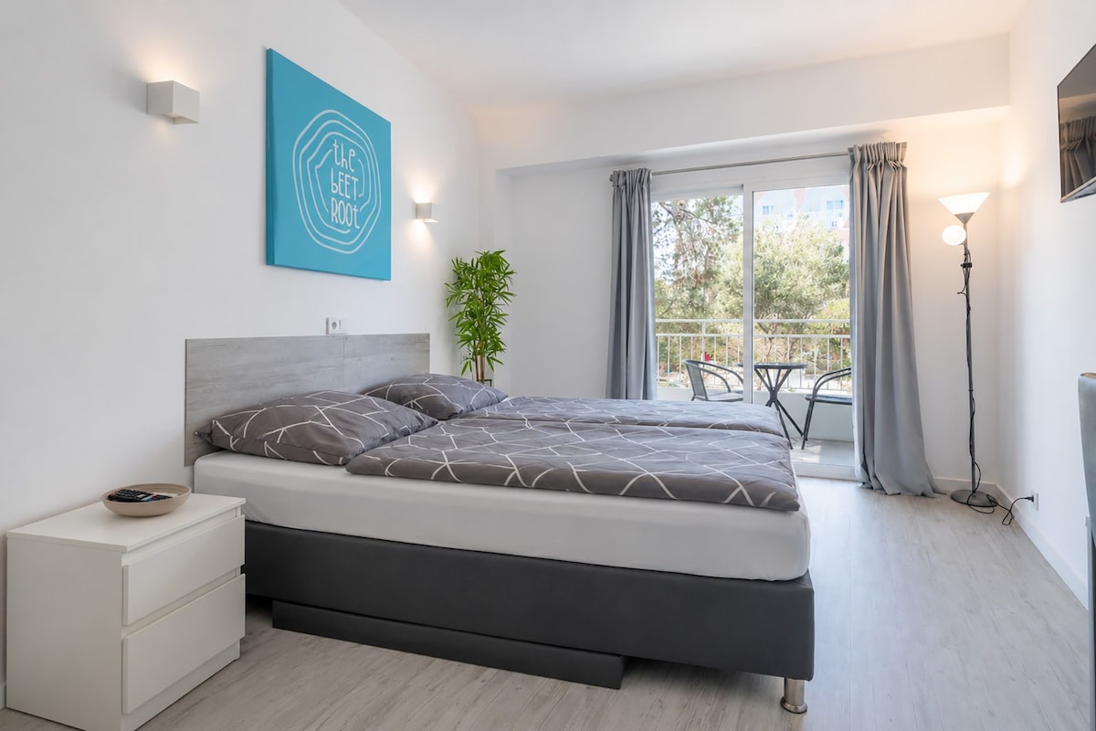 Quarto moderno com cama, mesa de cabeceira e vista para o exterior.