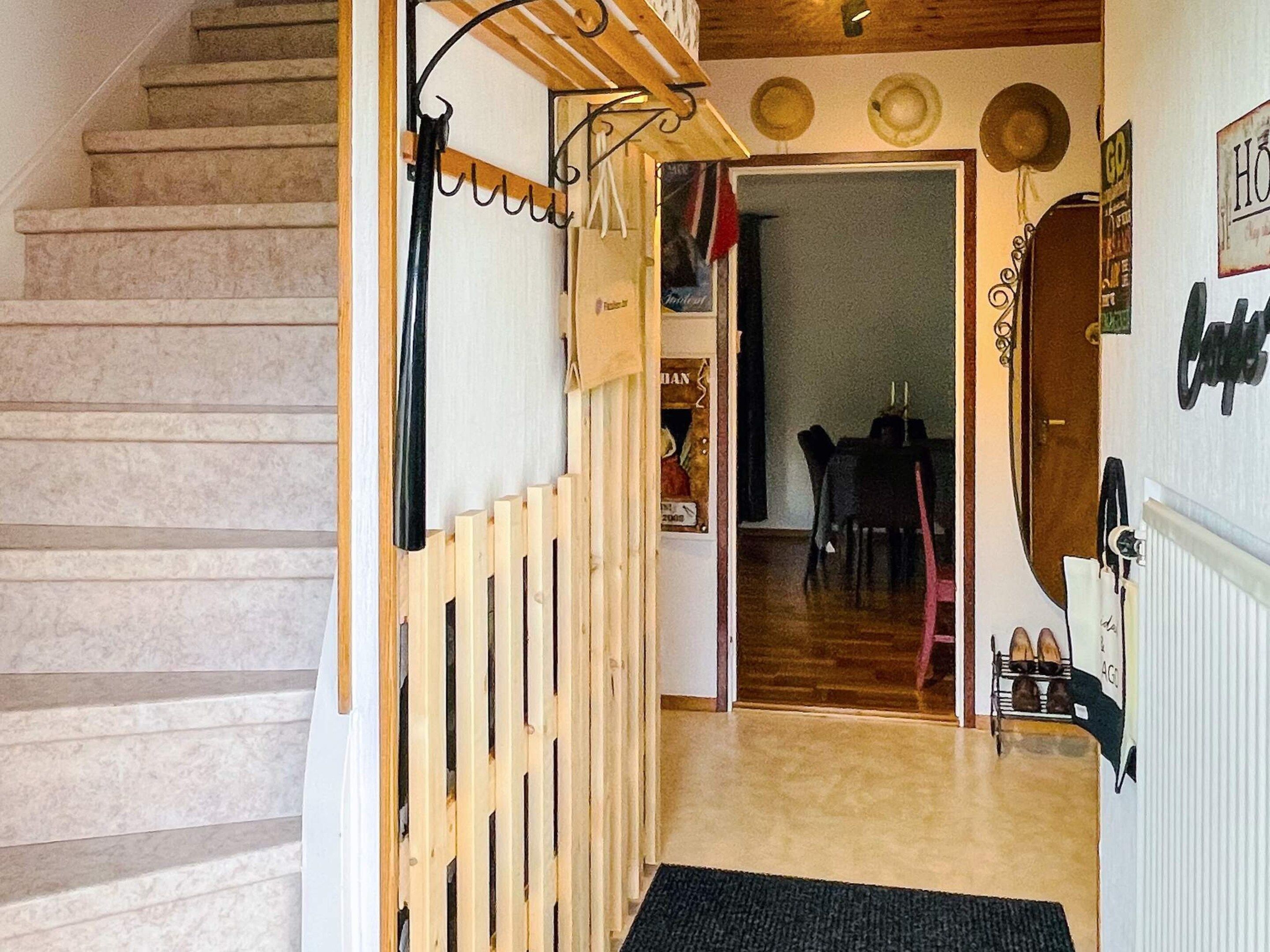 A staircase leading to a dining area with a table and chairs, a shoe rack, and a wall with a radiator and a mirror.
