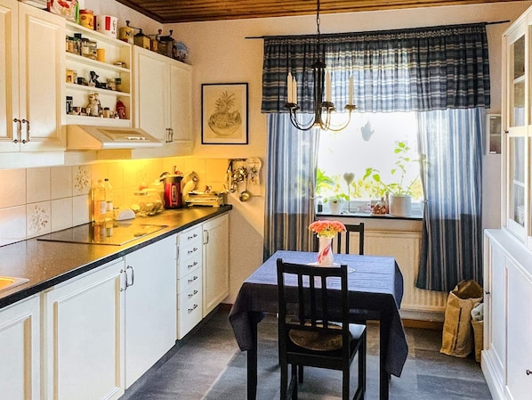 Cozinha com armários brancos, bancada preta, mesa de jantar e uma cadeira, além de um lustre.