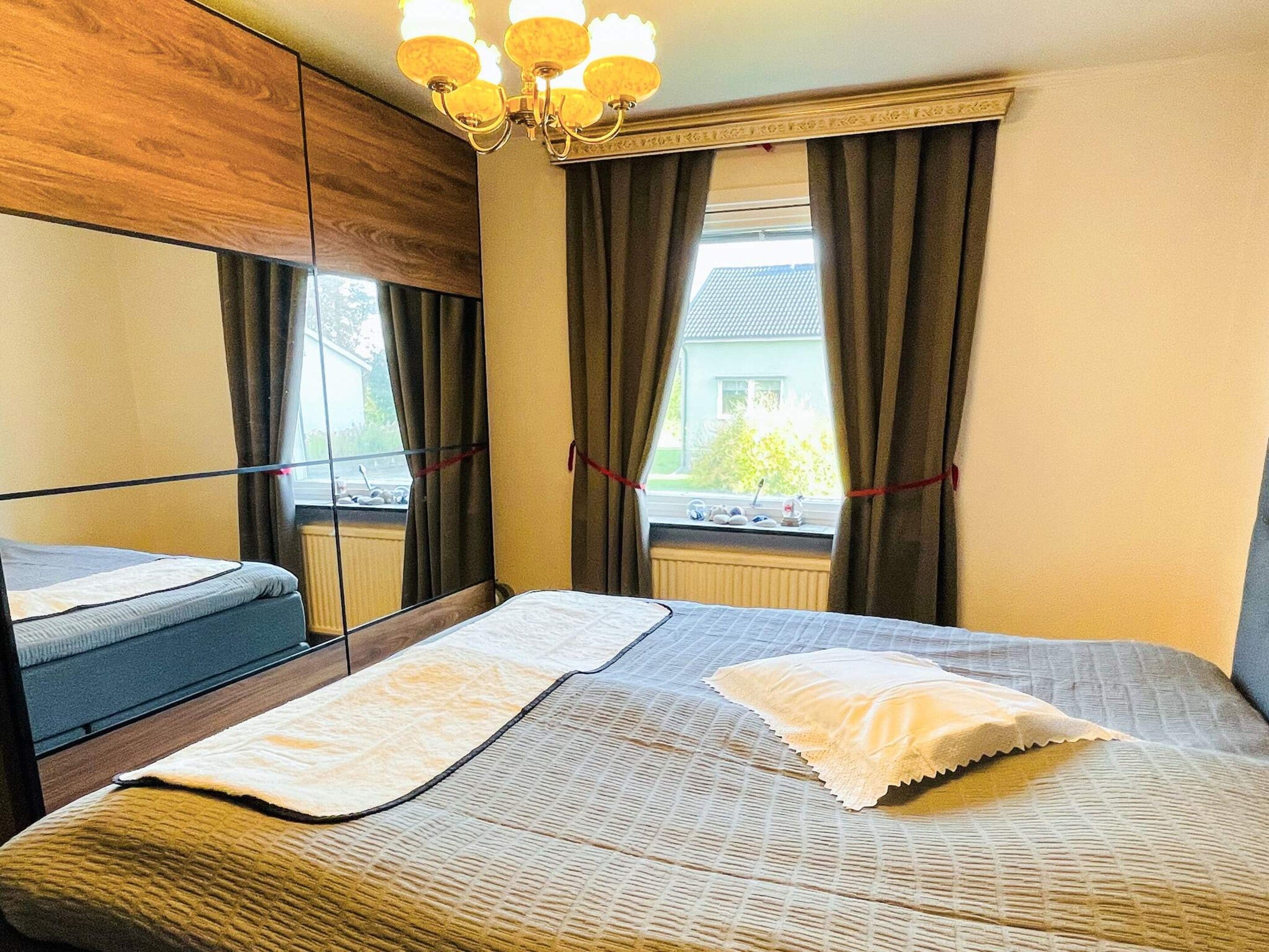 A hotel room with a bed, a window with curtains, a radiator, and a chandelier.
