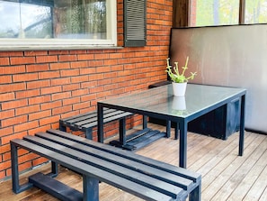 A patio area with a glass table and benches, a potted plant, and a brick wall. - 8 Person Holiday Home in Stockaryd (Stockaryd)
