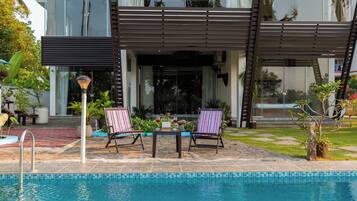Una zona junto a la piscina con dos sillones, una mesa y una piscina.