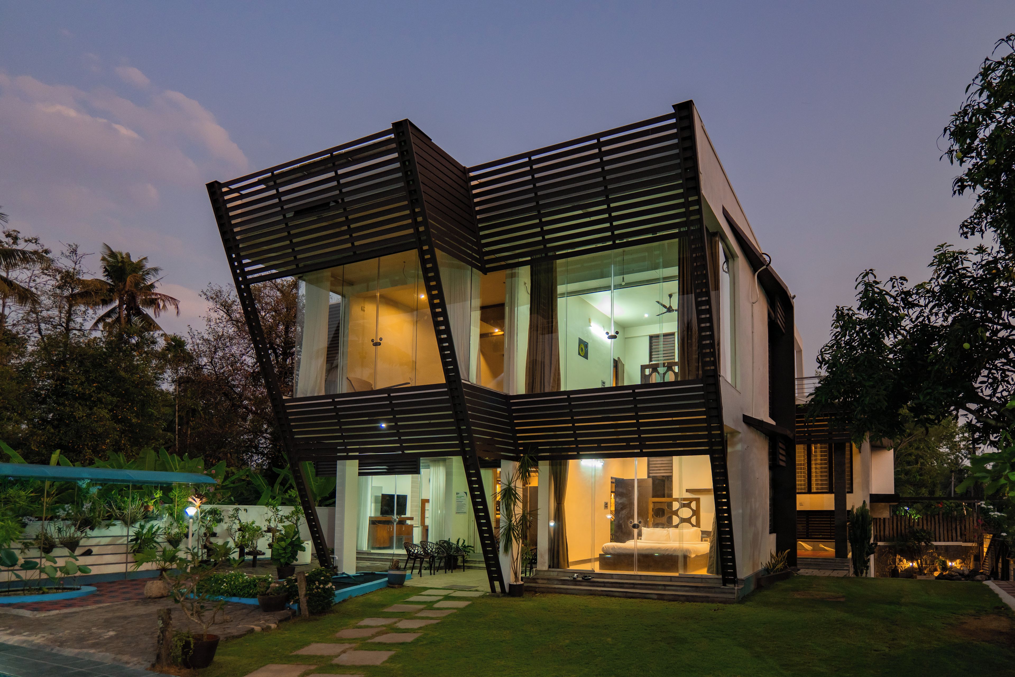Una casa moderna de dos plantas con fachada de vidrio, una escalera que conduce al nivel superior y un jardín bien cuidado.