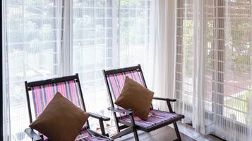 A room with two chairs, a ceiling with a unique design, and a view through large windows with sheer curtains.