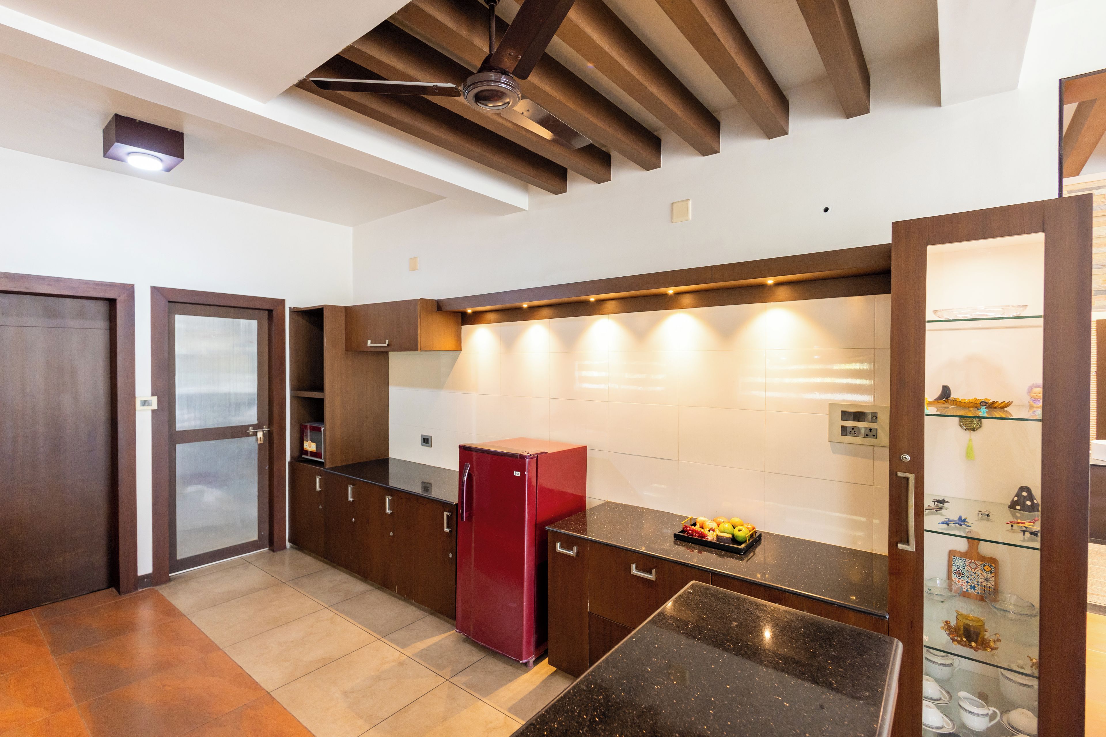Una cocina moderna con horno empotrado, un refrigerador rojo y una vitrina de vidrio.