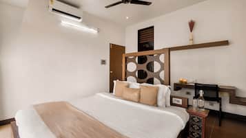 A modern hotel room with a large bed, a ceiling fan, an air conditioning unit, a bedside table with a lamp, and a decorative wall panel.