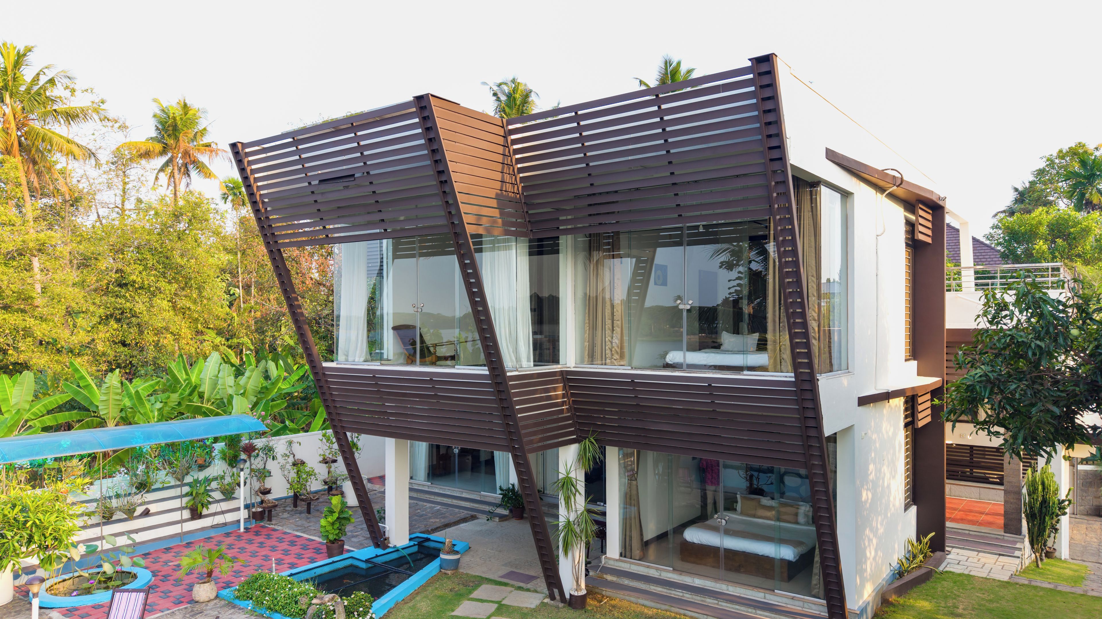A modern house with a unique slanted roof design, large glass windows, and a small outdoor garden area.