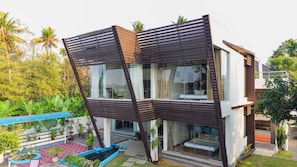 A modern house with a unique slanted roof design, large glass windows, and a small outdoor garden area. - Glass River Retreat (Aluva)