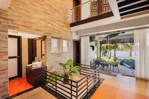 A modern interior with a stone wall, a round sink, and a view of a pool and greenery outside. - Glass River Retreat (Aluva)