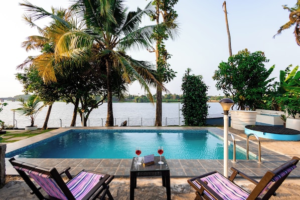 A swimming pool with lounge chairs and a table, surrounded by palm trees and a view of the water.